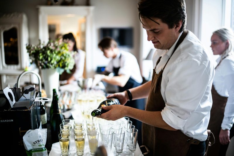 Waitstaff pouring champagne into glasses at a sophisticated indoor event.